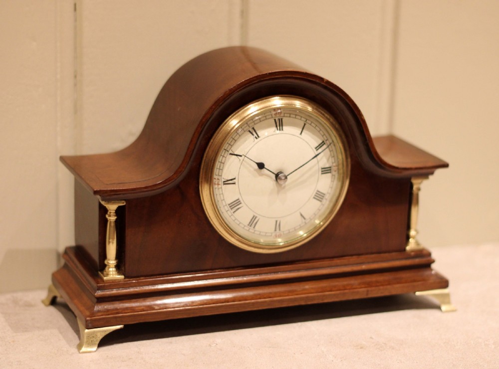An Edwardian mahogany mantel clock featuring an arched top, turned brass side columns, brass feet, and a white dial with Roman numerals. View II