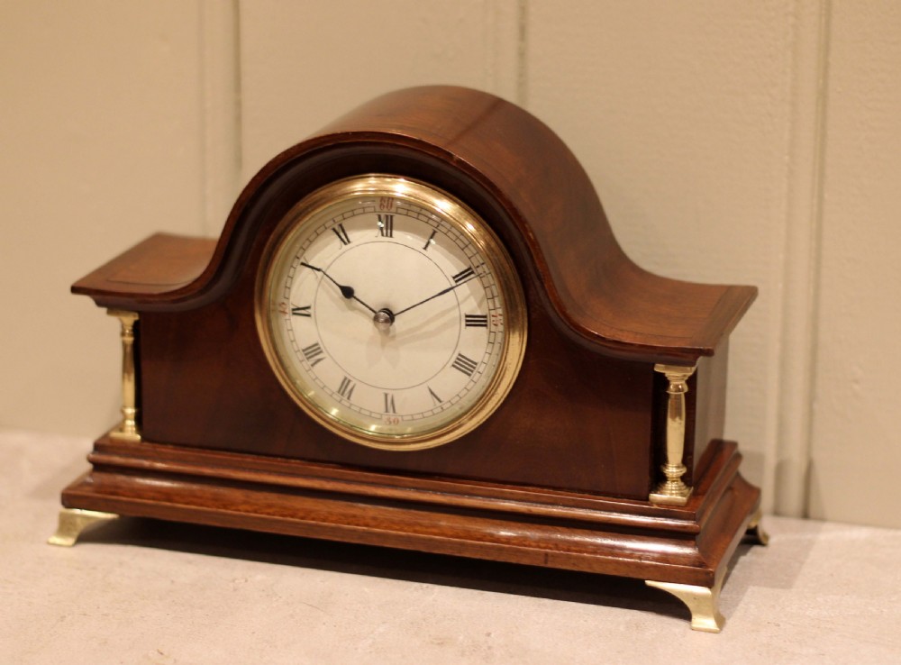 An Edwardian mahogany mantel clock featuring an arched top, turned brass side columns, brass feet, and a white dial with Roman numerals. View III