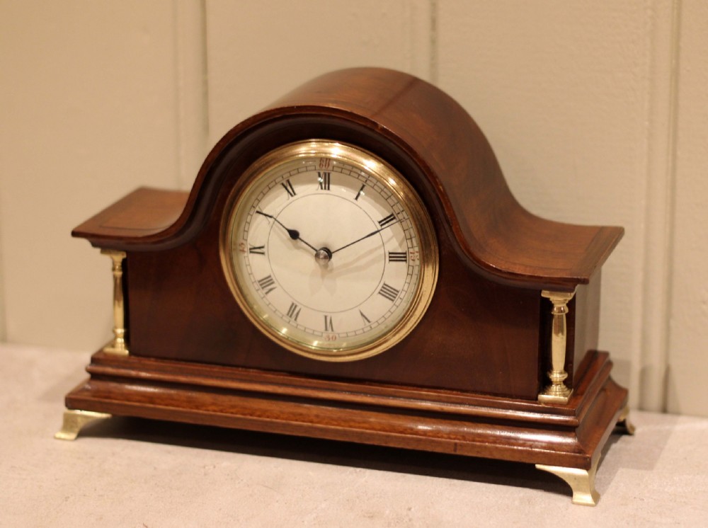 An Edwardian mahogany mantel clock featuring an arched top, turned brass side columns, brass feet, and a white dial with Roman numerals. View V