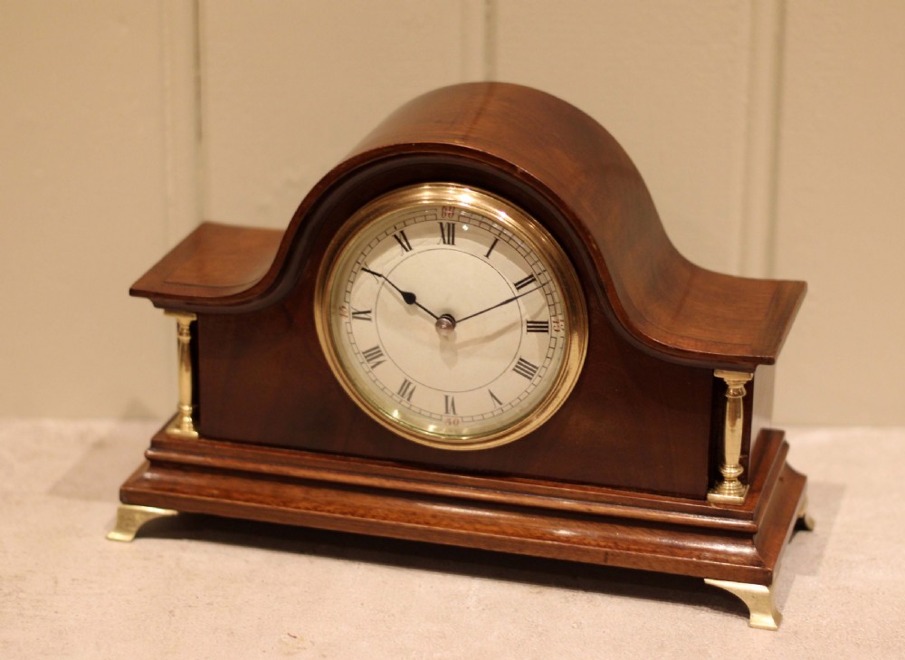 An Edwardian mahogany mantel clock featuring an arched top, turned brass side columns, brass feet, and a white dial with Roman numerals. View VII