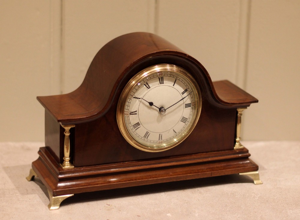 An Edwardian mahogany mantel clock featuring an arched top, turned brass side columns, brass feet, and a white dial with Roman numerals. View VIII