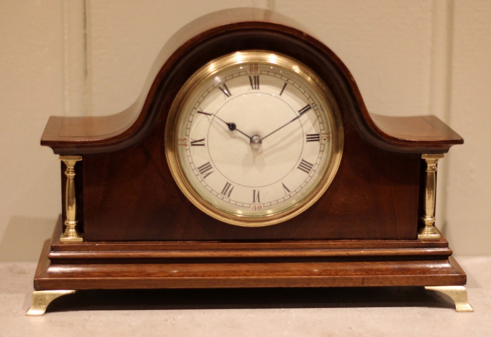 An Edwardian mahogany mantel clock featuring an arched top, turned brass side columns, brass feet, and a white dial with Roman numerals. View IX