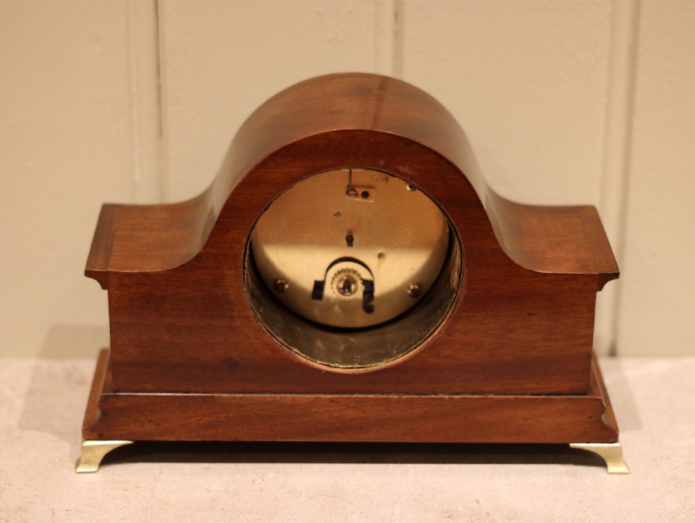 An Edwardian mahogany mantel clock featuring an arched top, turned brass side columns, brass feet, and a white dial with Roman numerals. View XI