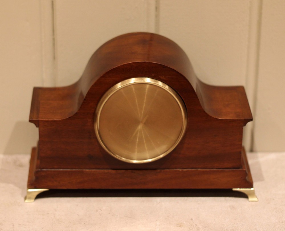 An Edwardian mahogany mantel clock featuring an arched top, turned brass side columns, brass feet, and a white dial with Roman numerals. View XII