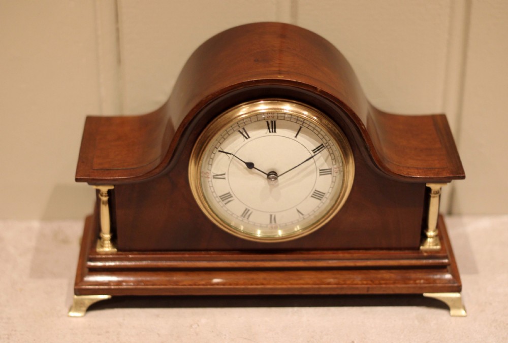 An Edwardian mahogany mantel clock featuring an arched top, turned brass side columns, brass feet, and a white dial with Roman numerals. View XIII