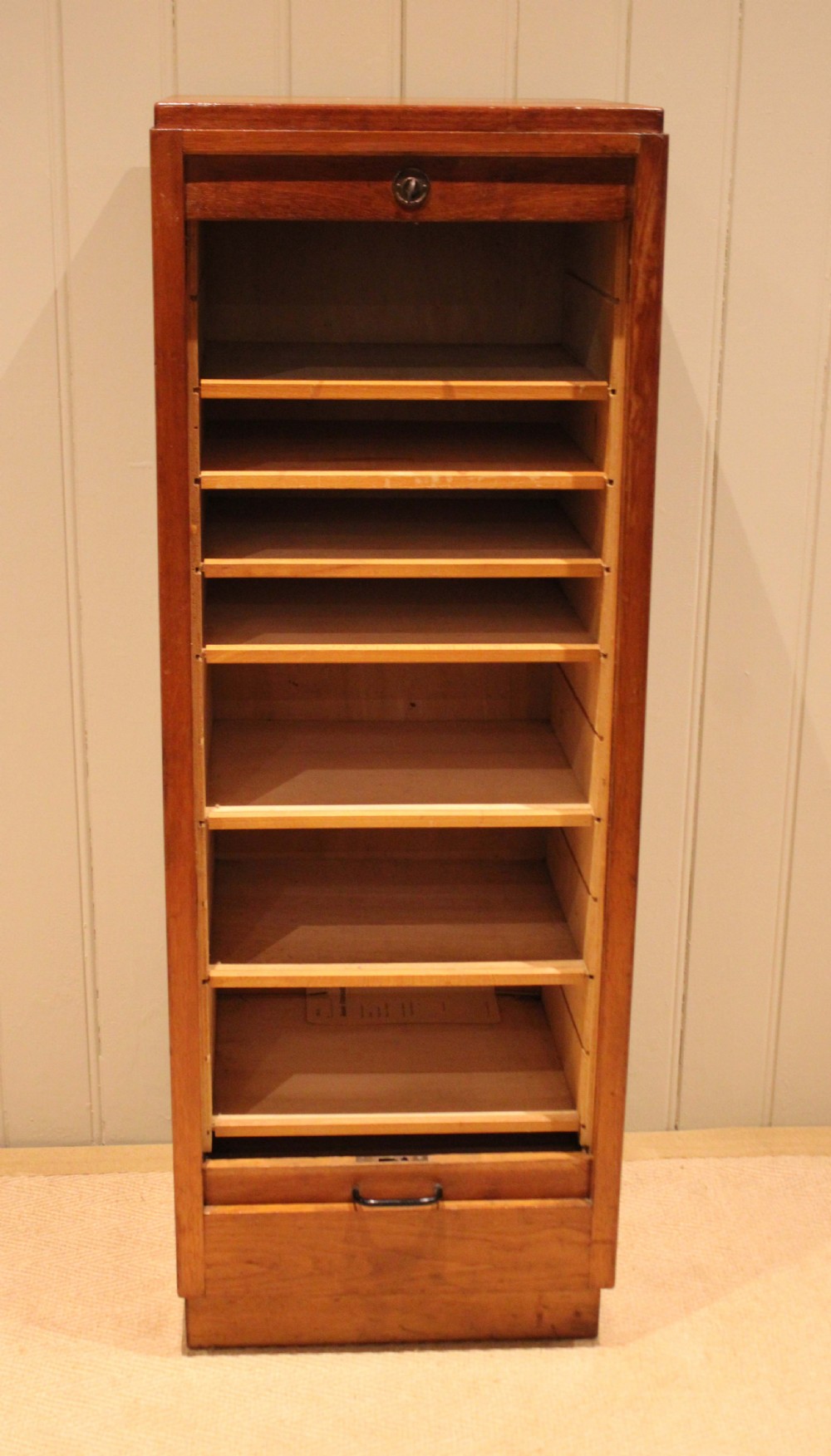 A tall, narrow antique oak filing cabinet with a vertical slatted tambour shutter front, top metal pull handle, and keyhole lock. View II