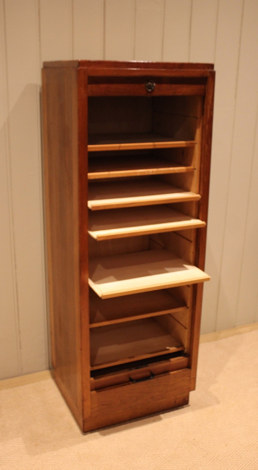 A tall, narrow antique oak filing cabinet with a vertical slatted tambour shutter front, top metal pull handle, and keyhole lock. View IV