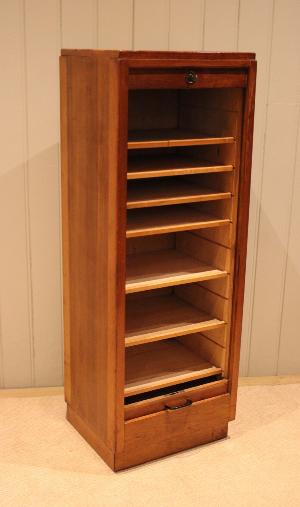 A tall, narrow antique oak filing cabinet with a vertical slatted tambour shutter front, top metal pull handle, and keyhole lock. View VI