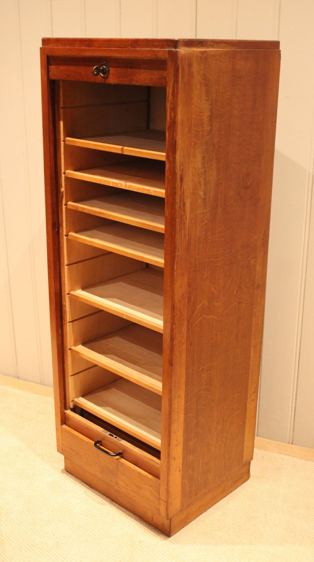 A tall, narrow antique oak filing cabinet with a vertical slatted tambour shutter front, top metal pull handle, and keyhole lock. View VIII