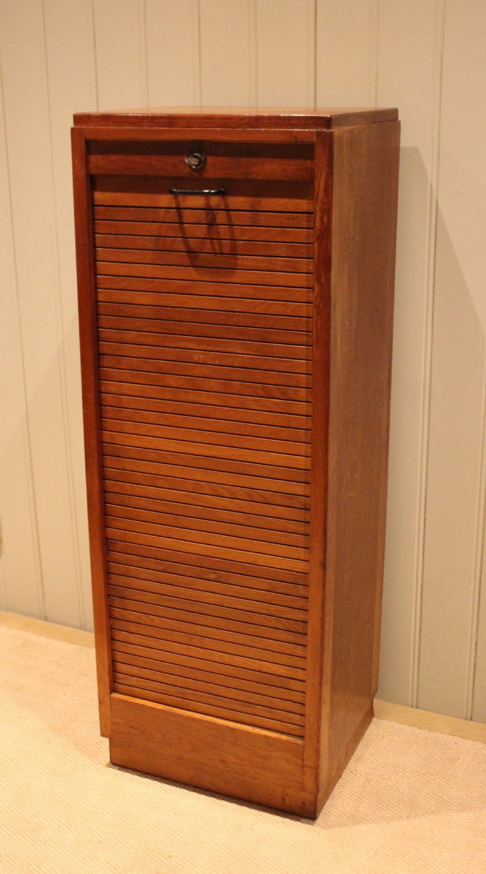 A tall, narrow antique oak filing cabinet with a vertical slatted tambour shutter front, top metal pull handle, and keyhole lock. View IX