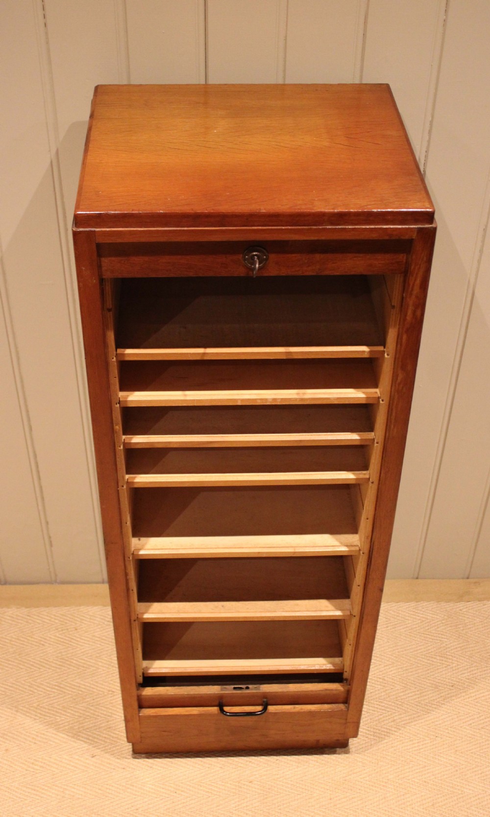 A tall, narrow antique oak filing cabinet with a vertical slatted tambour shutter front, top metal pull handle, and keyhole lock. View X