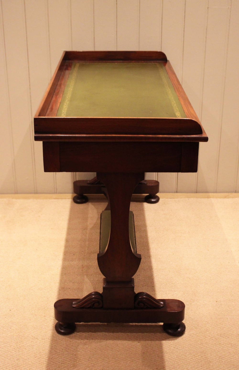 A mahogany writing table featuring a green gilt-tooled leather inset writing surface, a three-sided gallery rail, two drawers with brass ring pull handles, and a trestle base with a central footrest. View XI