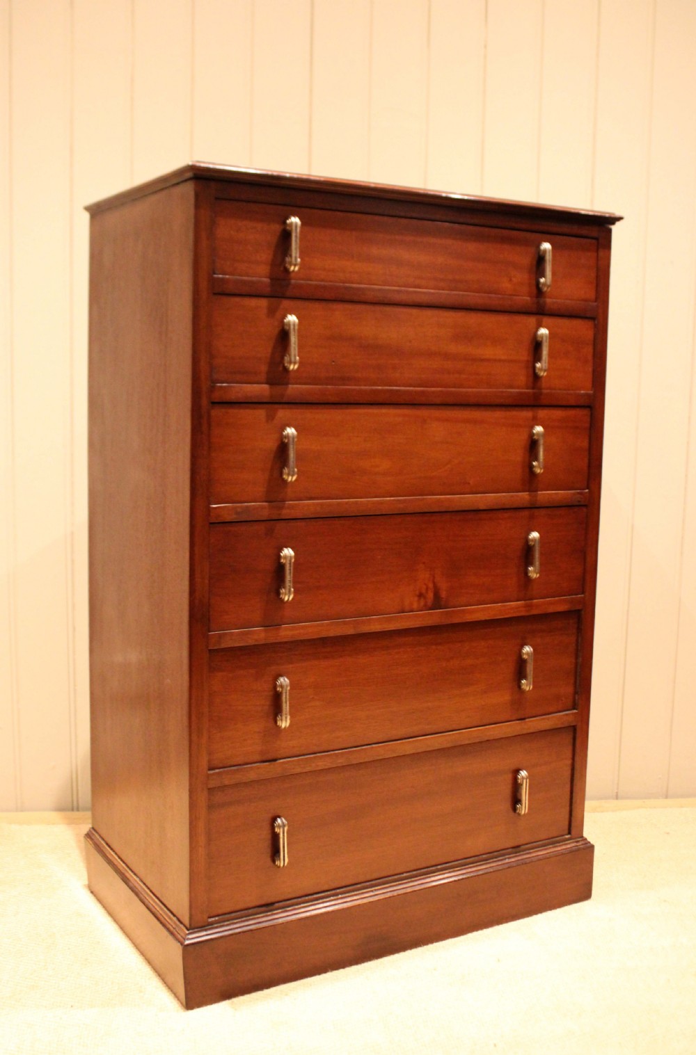 A tall mahogany chest of drawers featuring six horizontal drawers with vertical metal drop handles on a plinth base.