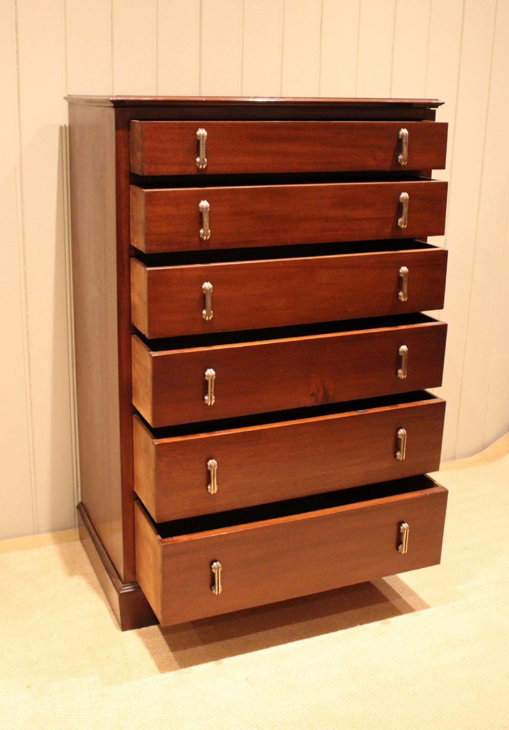 A tall mahogany chest of drawers featuring six horizontal drawers with vertical metal drop handles on a plinth base. View III