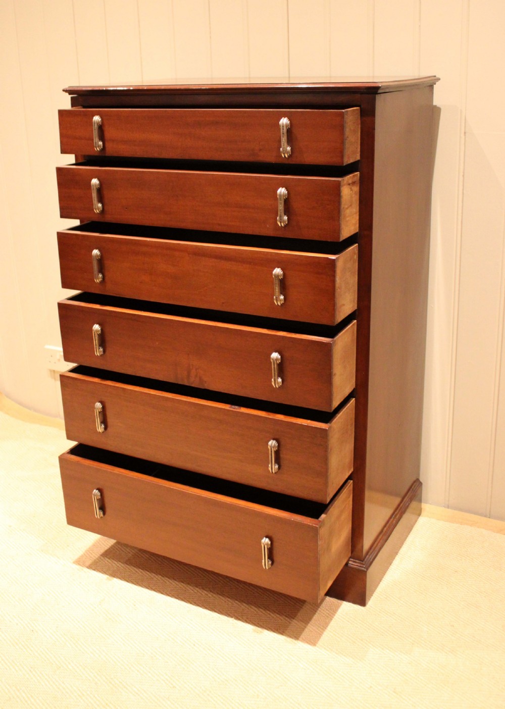 A tall mahogany chest of drawers featuring six horizontal drawers with vertical metal drop handles on a plinth base. View IV