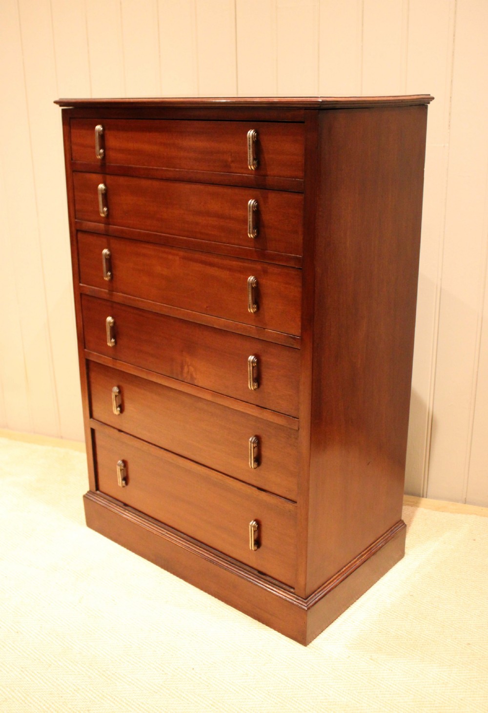 A tall mahogany chest of drawers featuring six horizontal drawers with vertical metal drop handles on a plinth base. View VI