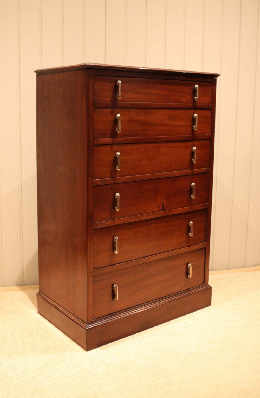 A tall mahogany chest of drawers featuring six horizontal drawers with vertical metal drop handles on a plinth base. View VII