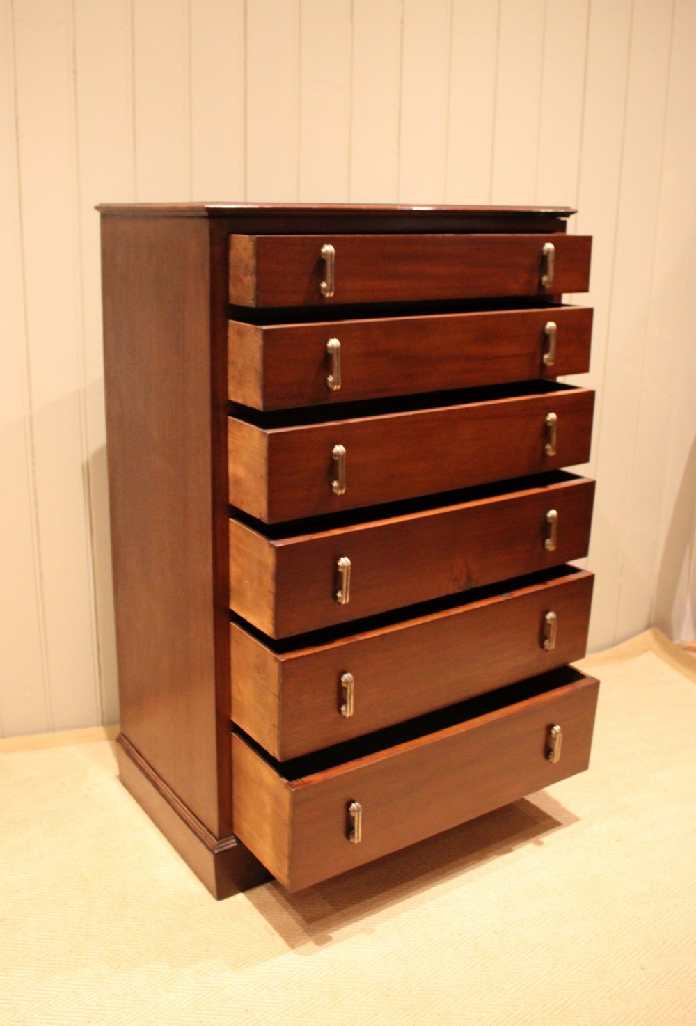 A tall mahogany chest of drawers featuring six horizontal drawers with vertical metal drop handles on a plinth base. View VIII