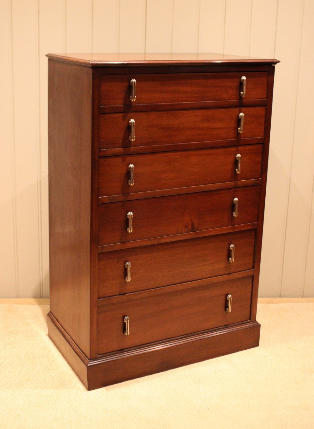 A tall mahogany chest of drawers featuring six horizontal drawers with vertical metal drop handles on a plinth base. View X