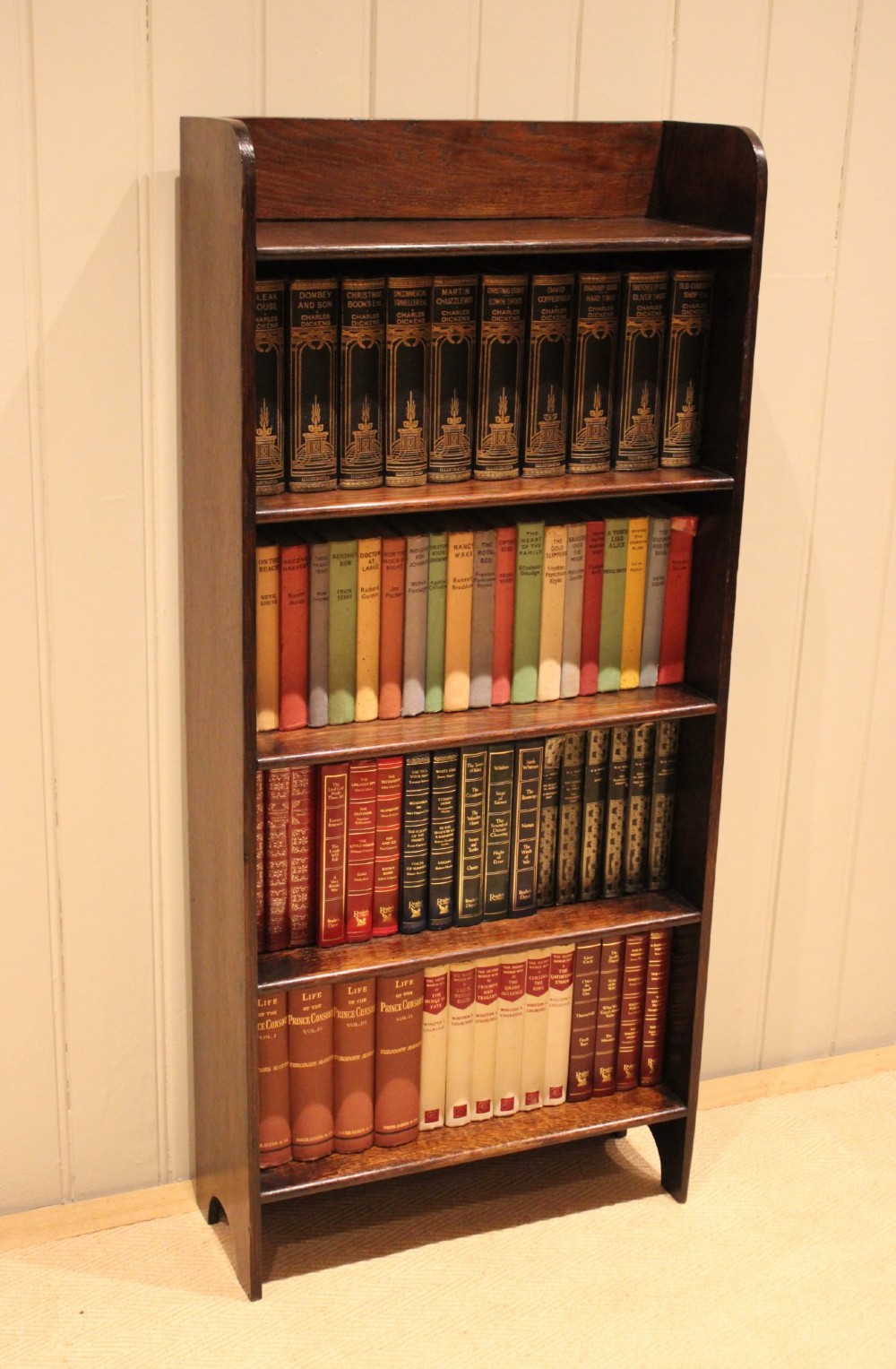 A tall dark oak open bookcase with four fixed shelves and shaped side profile cut-outs at the base.