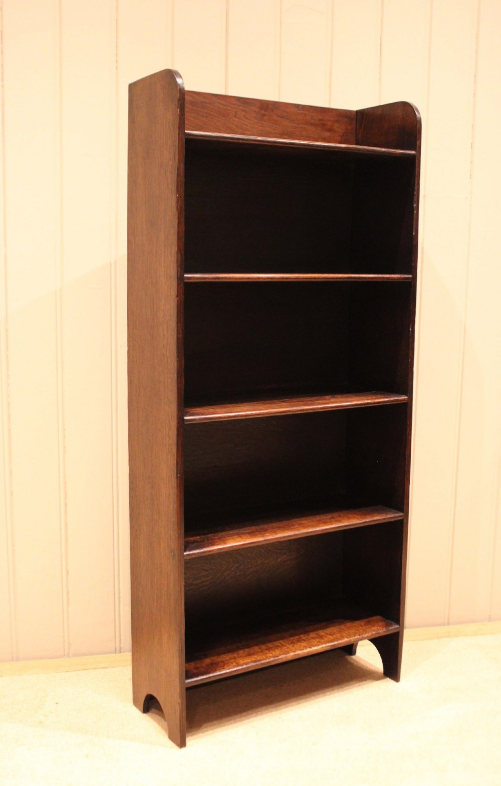 A tall dark oak open bookcase with four fixed shelves and shaped side profile cut-outs at the base. View VI
