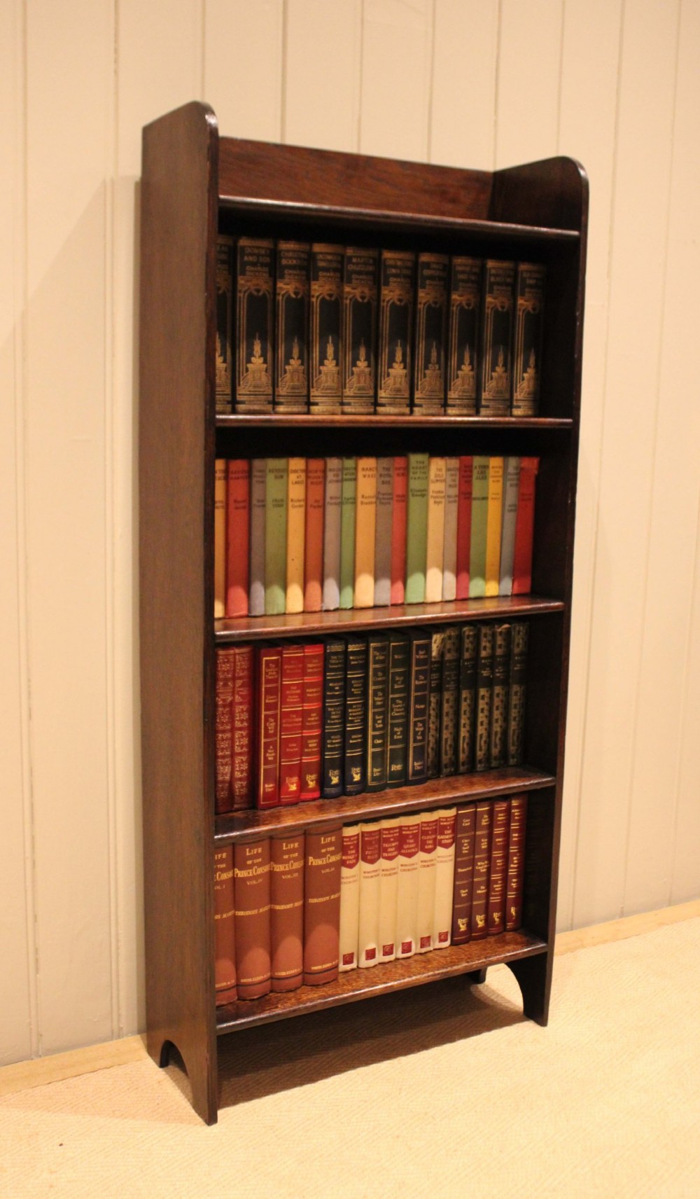 A tall dark oak open bookcase with four fixed shelves and shaped side profile cut-outs at the base. View VII