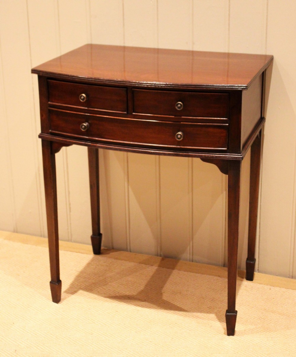 An Edwardian mahogany bow-front side table with drawers and brass handles resting on tapered legs. View III