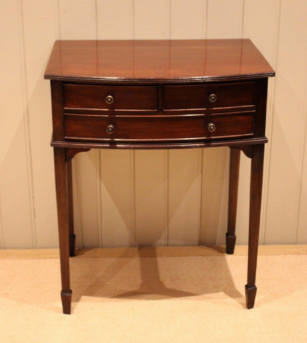 An Edwardian mahogany bow-front side table with drawers and brass handles resting on tapered legs. View IV