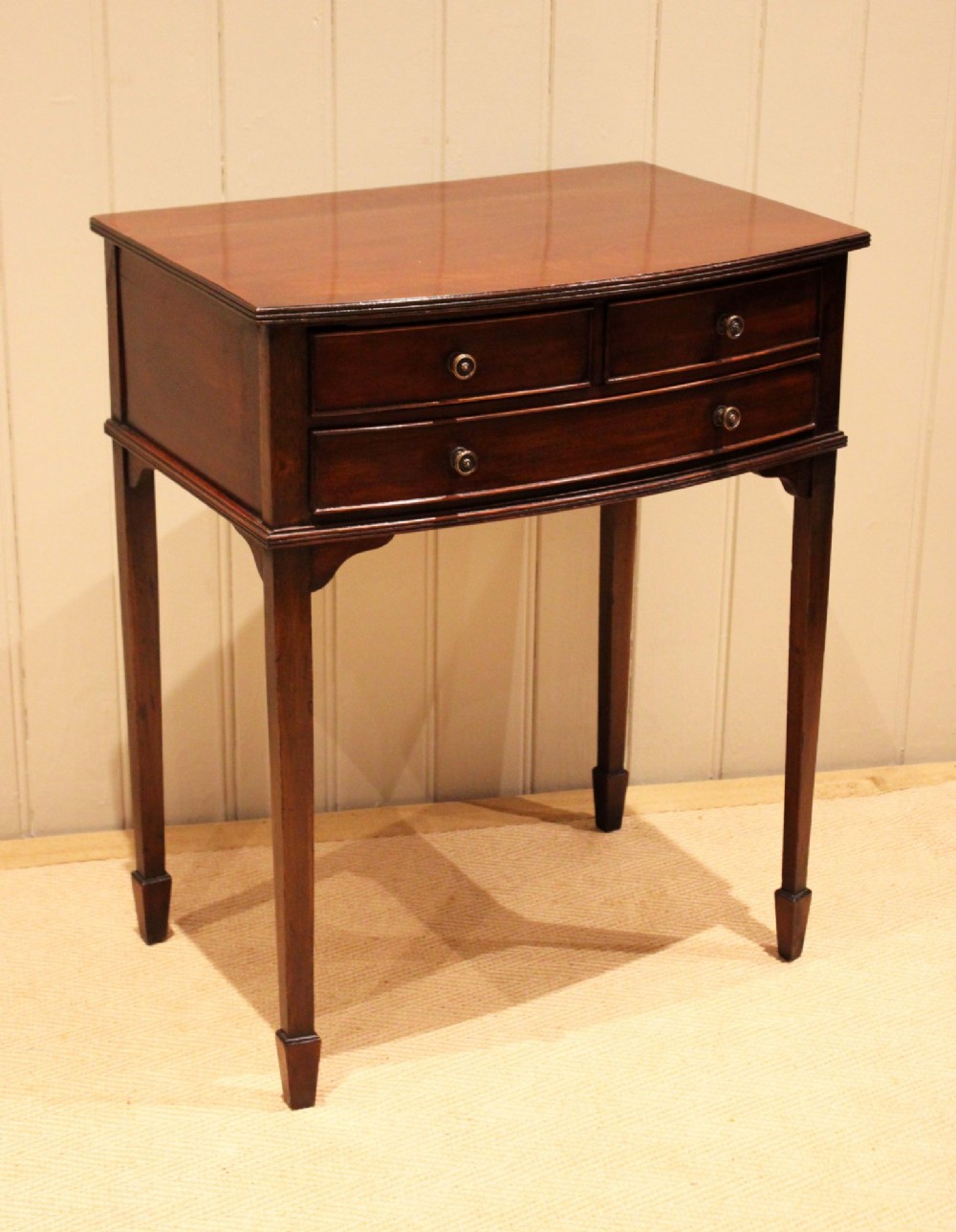 An Edwardian mahogany bow-front side table with drawers and brass handles resting on tapered legs. View V