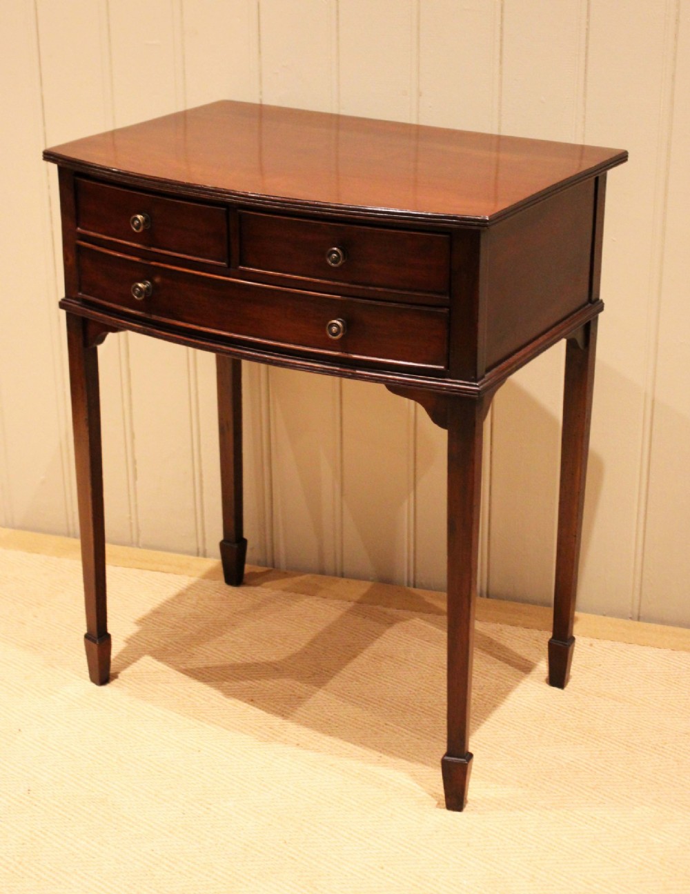 An Edwardian mahogany bow-front side table with drawers and brass handles resting on tapered legs. View VI