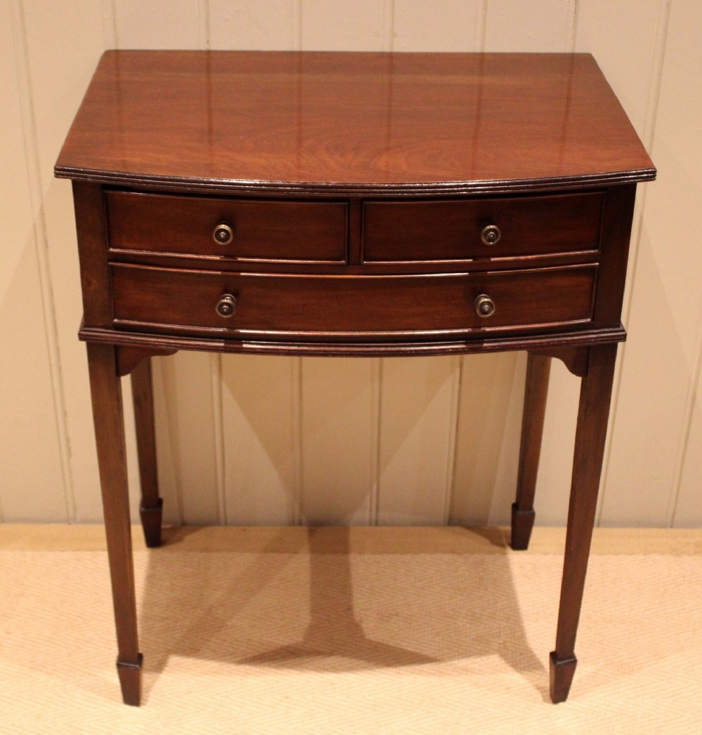 An Edwardian mahogany bow-front side table with drawers and brass handles resting on tapered legs. View VII