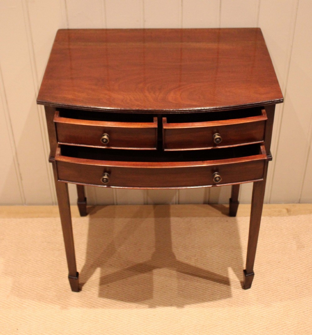 An Edwardian mahogany bow-front side table with drawers and brass handles resting on tapered legs. View VIII