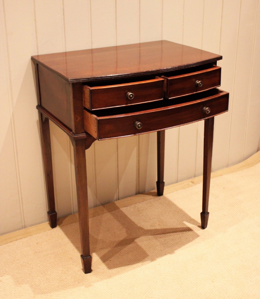 An Edwardian mahogany bow-front side table with drawers and brass handles resting on tapered legs. View X