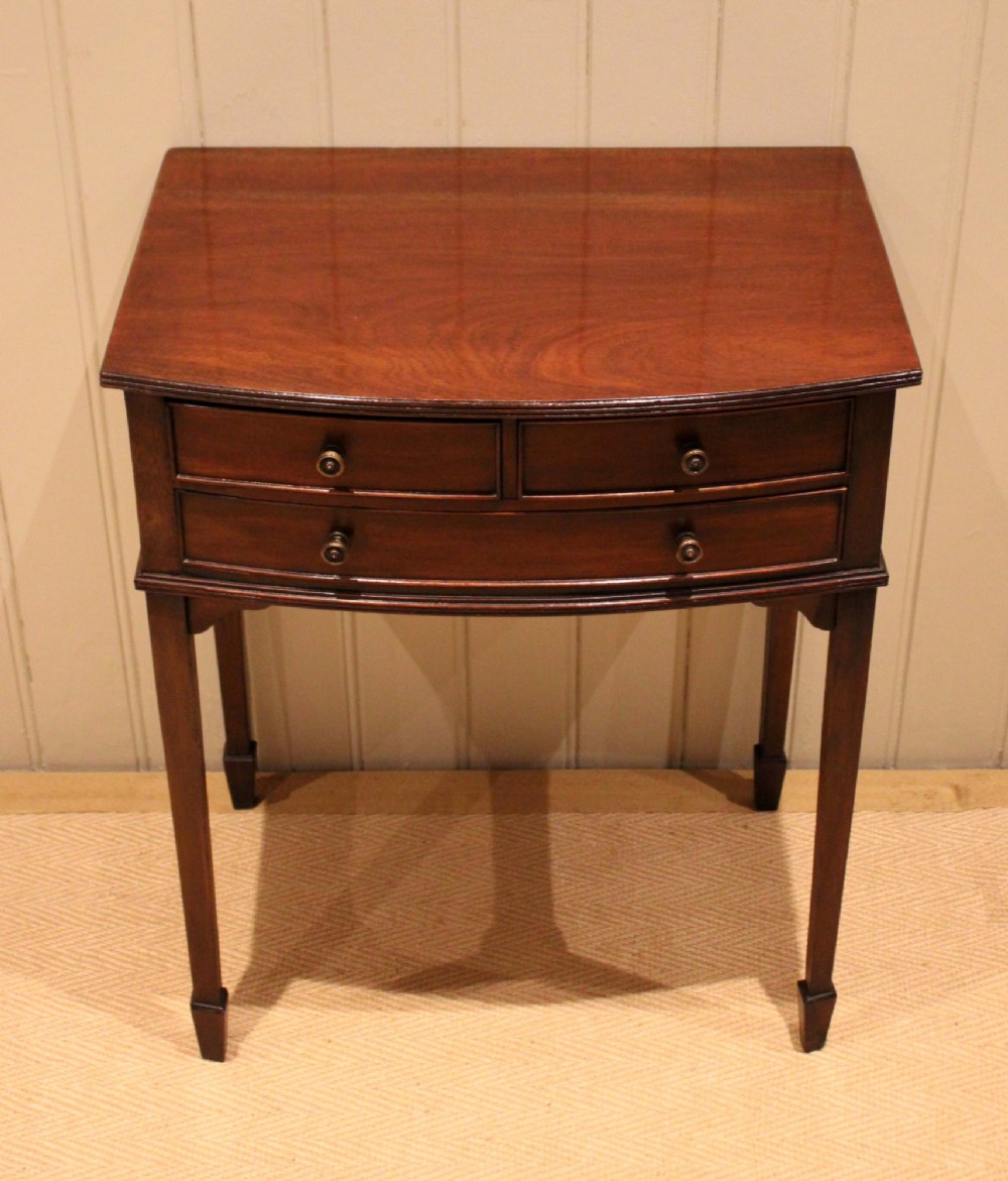 An Edwardian mahogany bow-front side table with drawers and brass handles resting on tapered legs. View XI