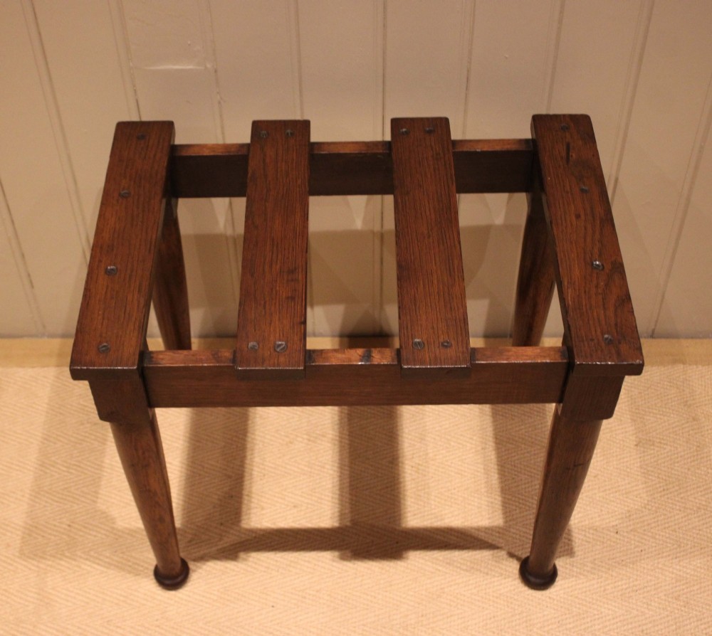 A solid dark oak luggage stand featuring a four-slat top surface supported by four turned tapered legs.