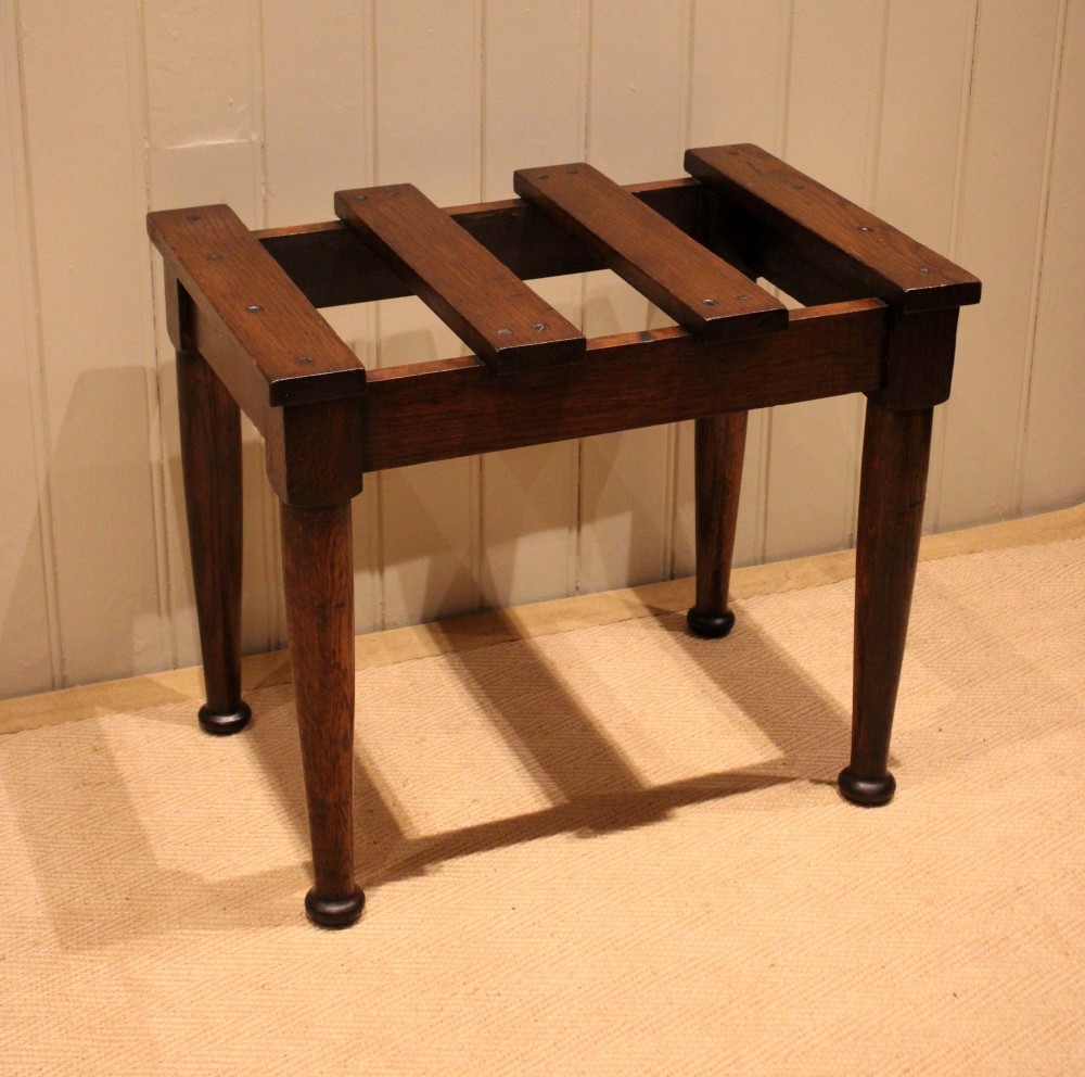 A solid dark oak luggage stand featuring a four-slat top surface supported by four turned tapered legs. View IV