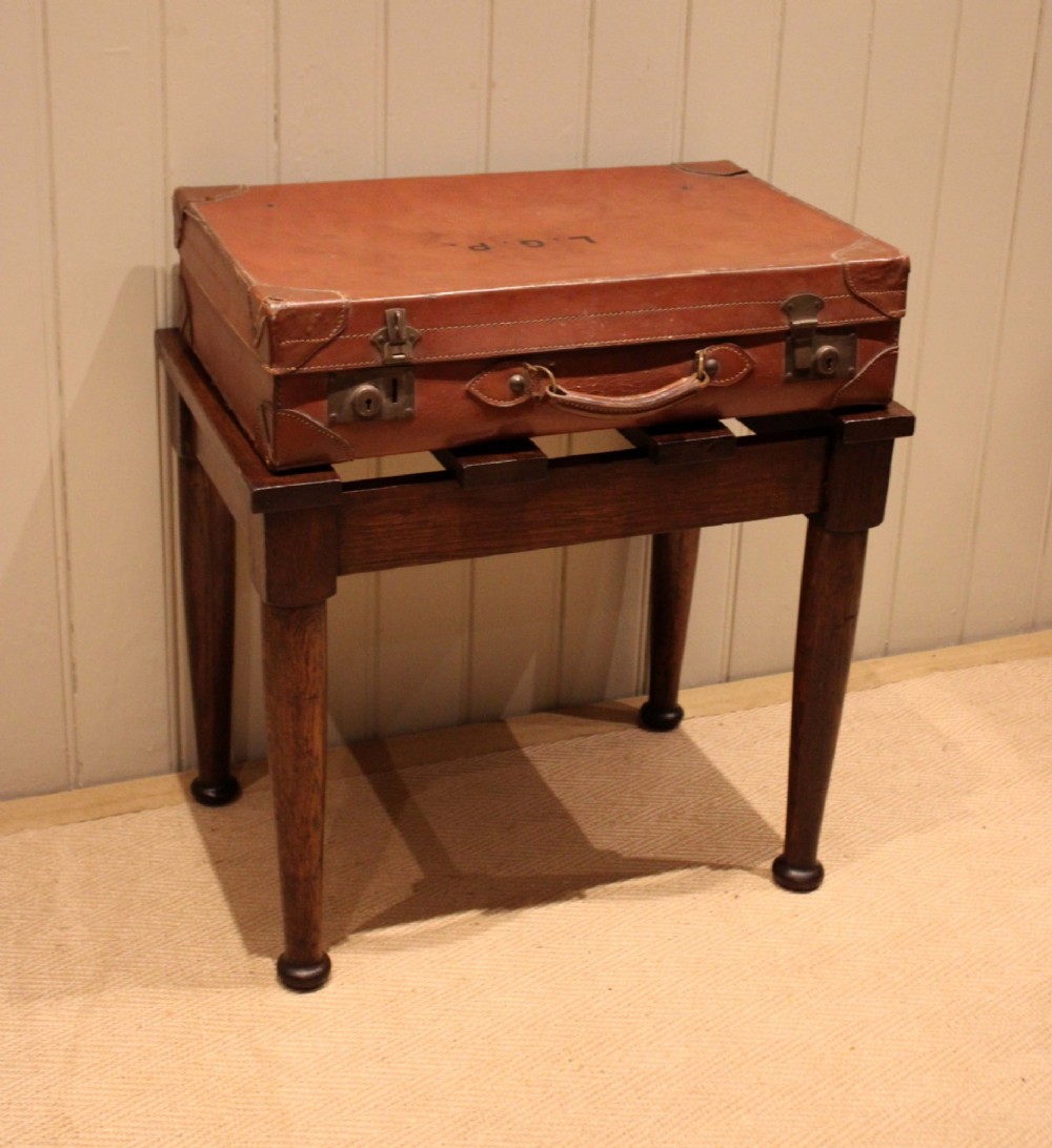 A solid dark oak luggage stand featuring a four-slat top surface supported by four turned tapered legs. View V