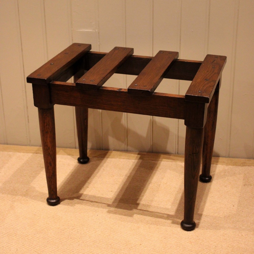 A solid dark oak luggage stand featuring a four-slat top surface supported by four turned tapered legs. View VII