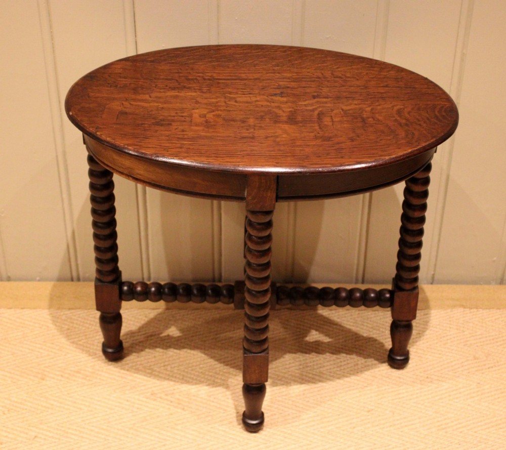 An antique dark oak side table featuring a smooth oval top supported by four bobbin-turned legs and matching low stretchers.