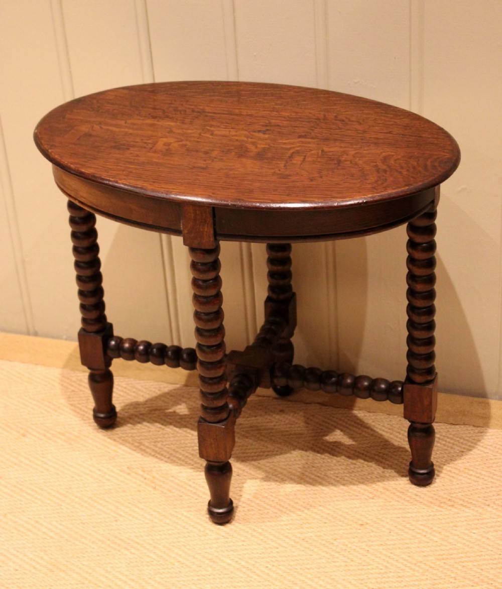 An antique dark oak side table featuring a smooth oval top supported by four bobbin-turned legs and matching low stretchers. View III