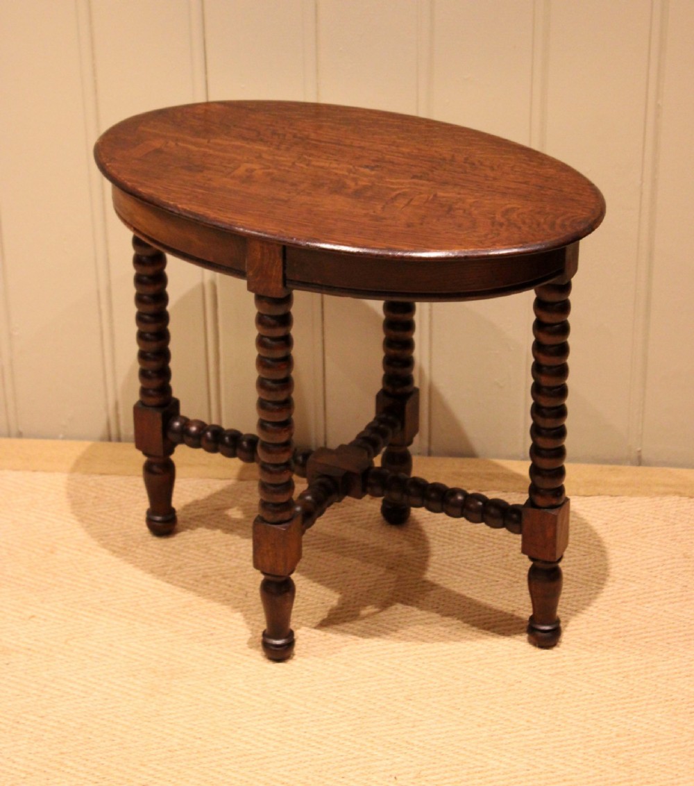 An antique dark oak side table featuring a smooth oval top supported by four bobbin-turned legs and matching low stretchers. View VI