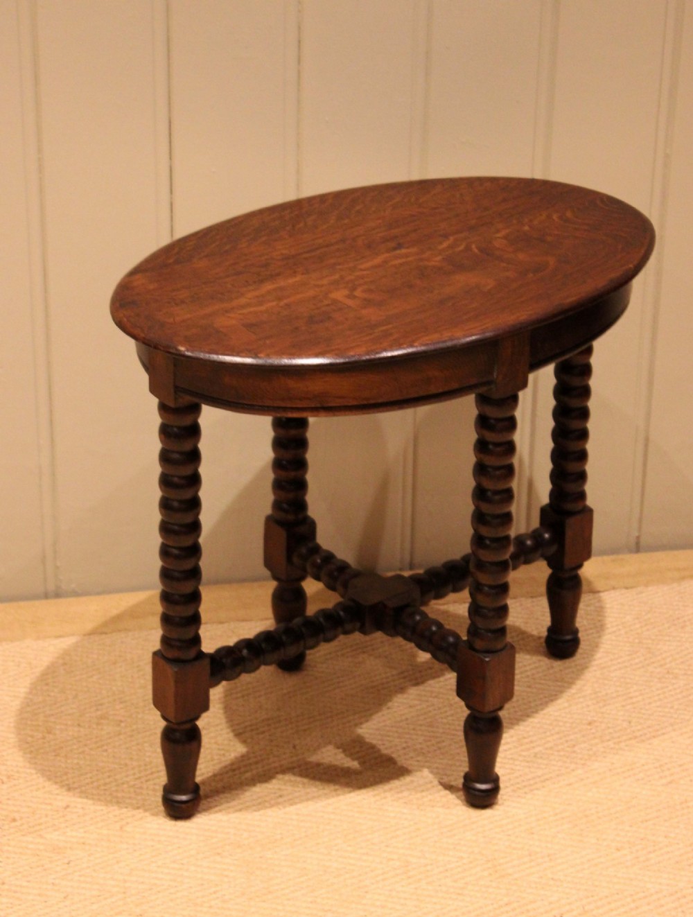 An antique dark oak side table featuring a smooth oval top supported by four bobbin-turned legs and matching low stretchers. View VII