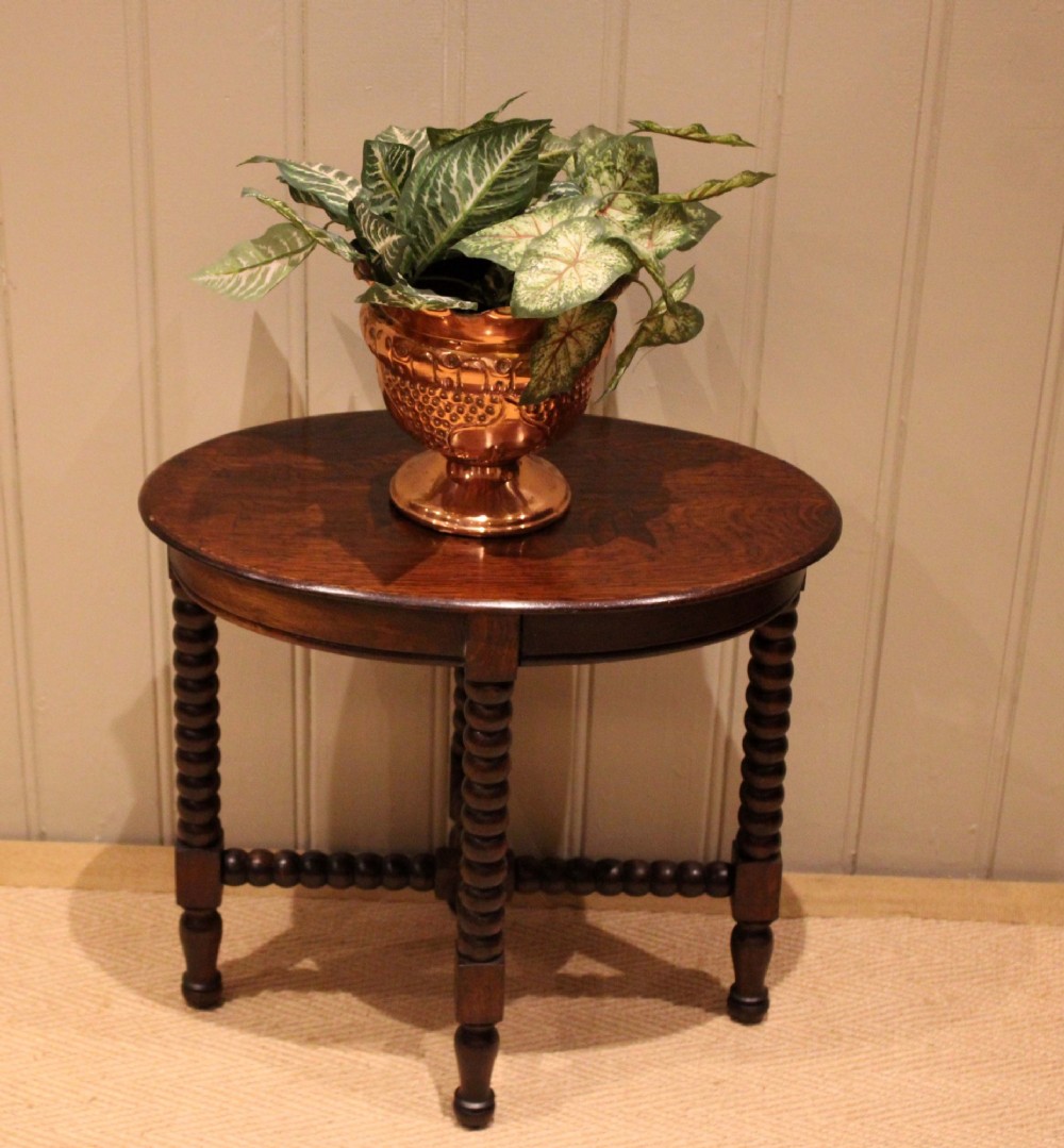 An antique dark oak side table featuring a smooth oval top supported by four bobbin-turned legs and matching low stretchers. View X