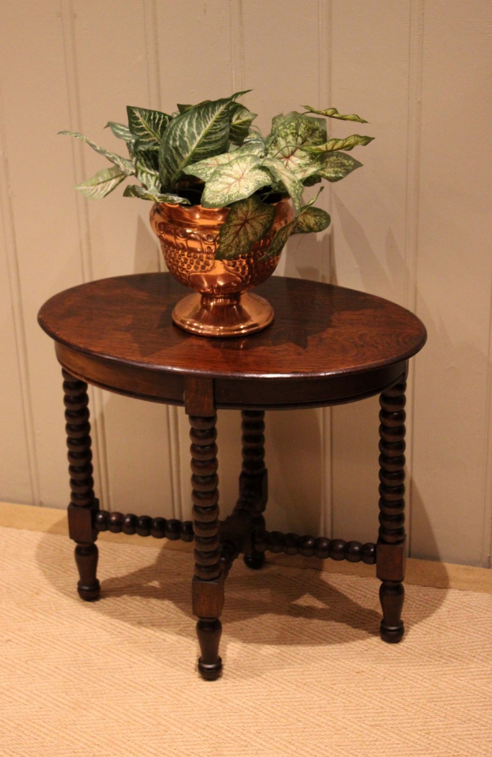An antique dark oak side table featuring a smooth oval top supported by four bobbin-turned legs and matching low stretchers. View XII