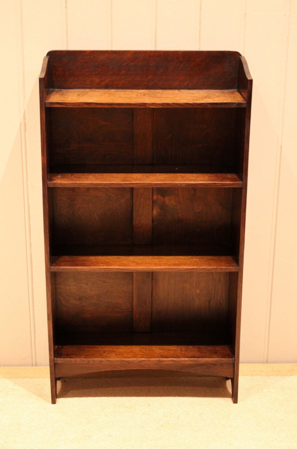A small dark oak open bookcase with three horizontal shelves filled with vintage books and a shaped top gallery. View II
