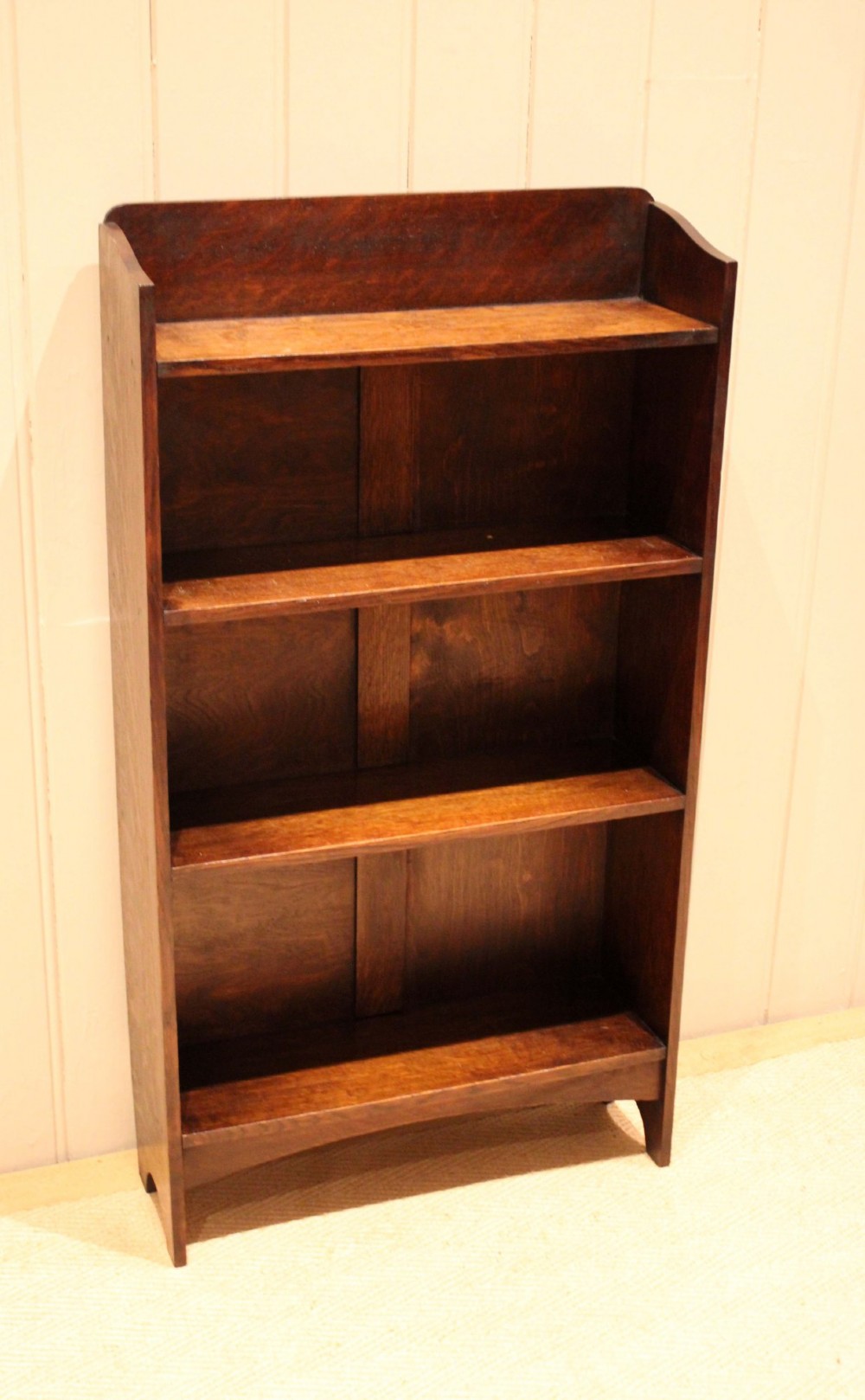 A small dark oak open bookcase with three horizontal shelves filled with vintage books and a shaped top gallery. View IV