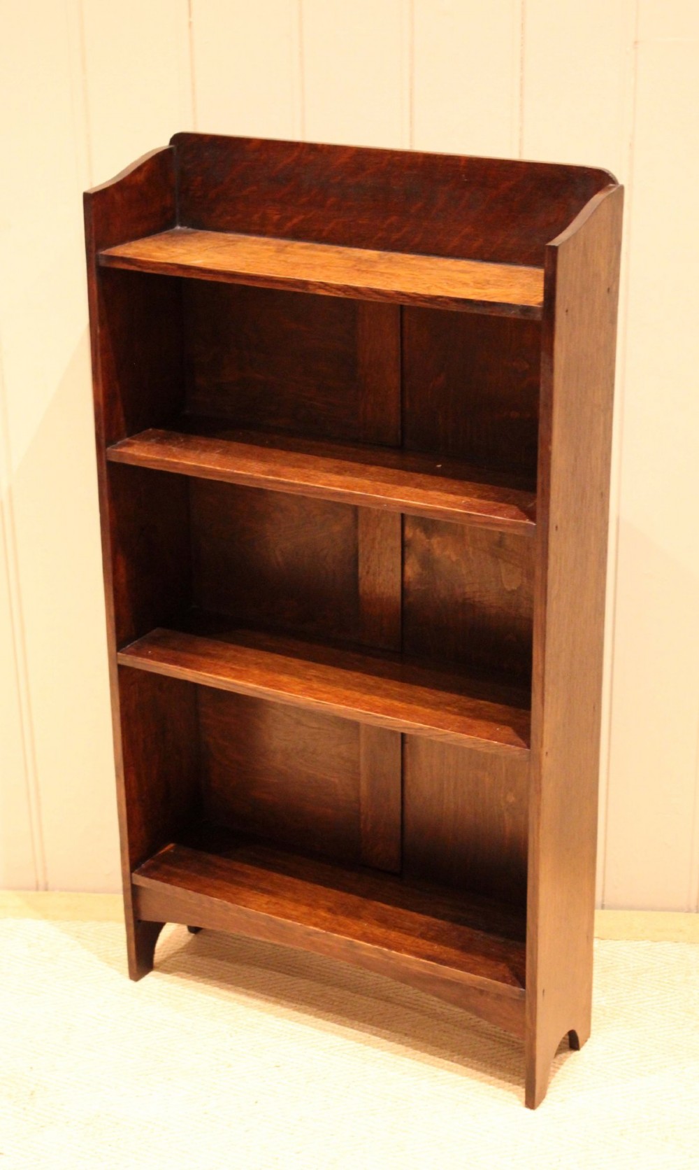A small dark oak open bookcase with three horizontal shelves filled with vintage books and a shaped top gallery. View VI