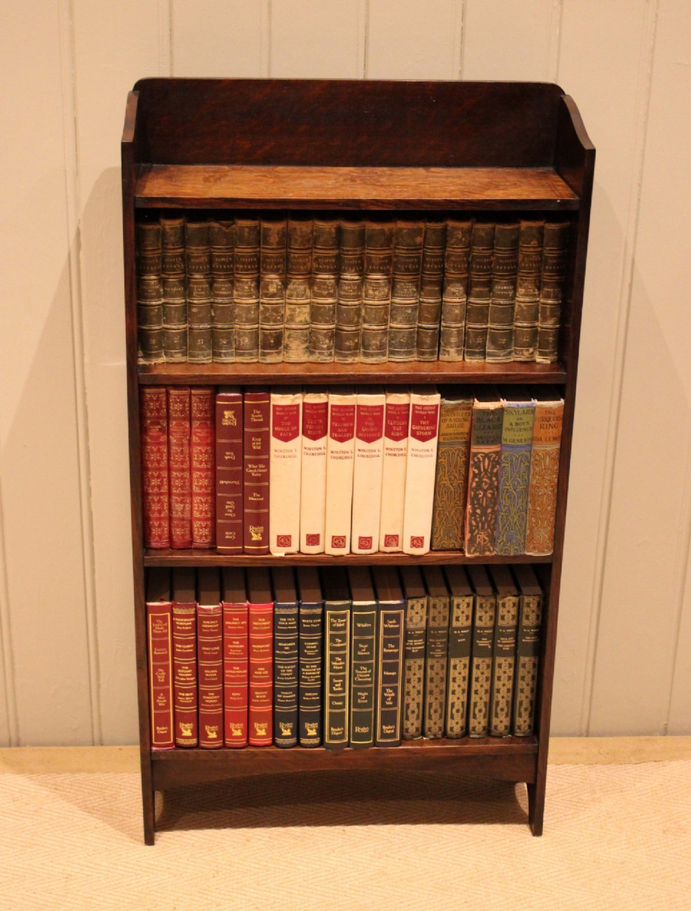 A small dark oak open bookcase with three horizontal shelves filled with vintage books and a shaped top gallery. View VII