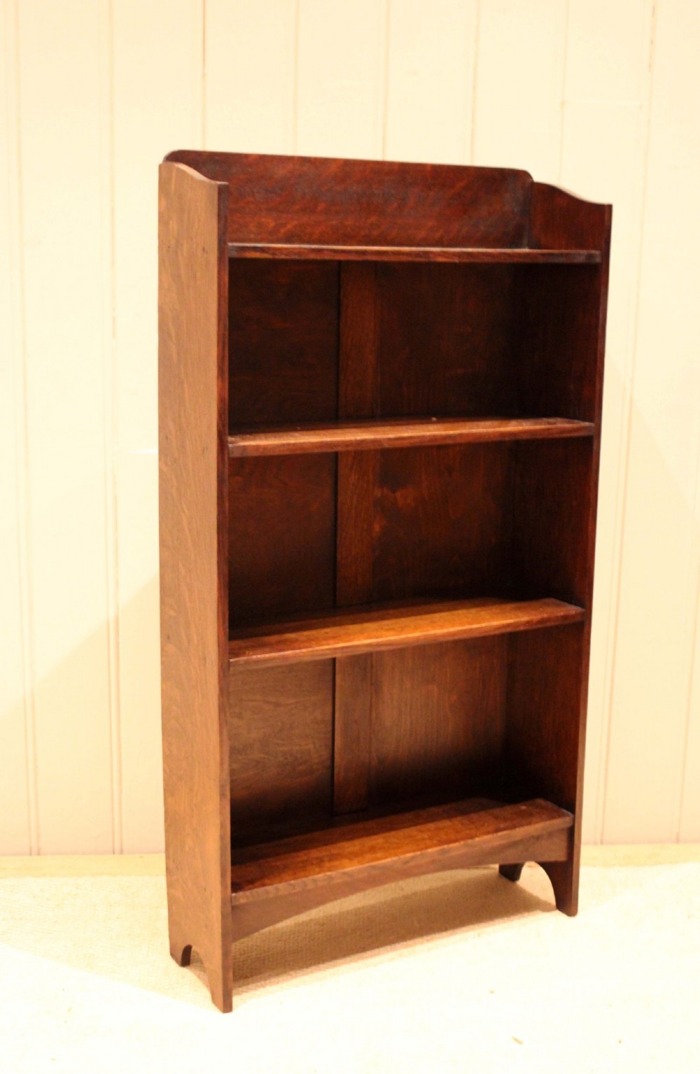 A small dark oak open bookcase with three horizontal shelves filled with vintage books and a shaped top gallery. View VIII