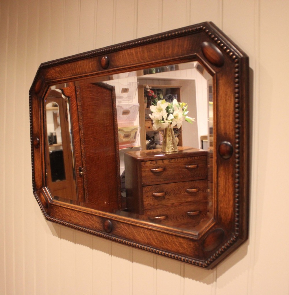 A large rectangular oak wall mirror with canted corners, beaded outer moulding, carved oval bosses, and a bevelled glass plate.